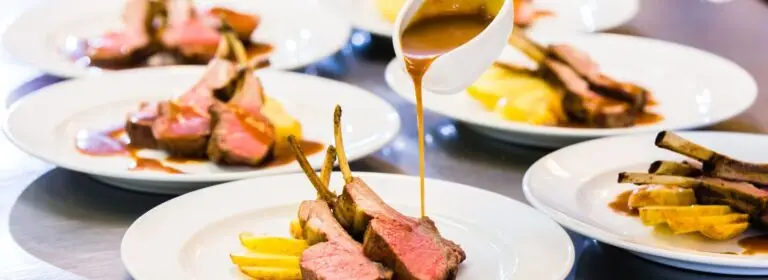 Sliced rack of lamb with gravy and roasted vegetables, plated by Pure Catering
