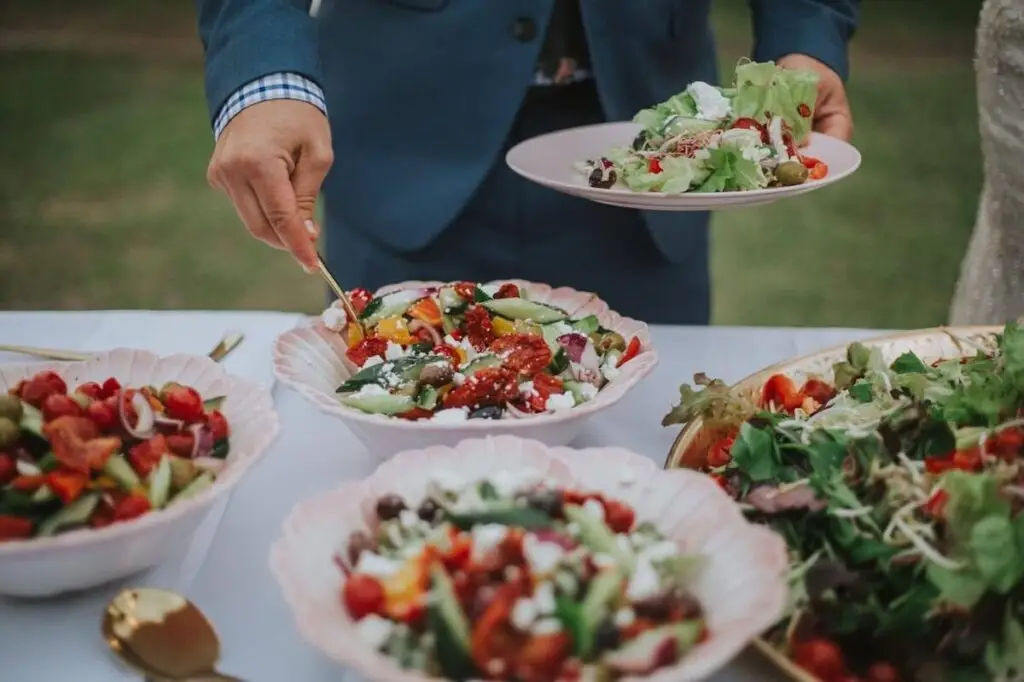 Caterer serving fresh salad from bowls at an outdoor table