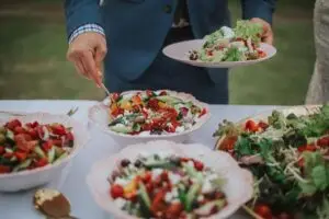 Caterer serving fresh salad from bowls at an outdoor table
